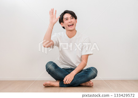 A young Asian man sitting cross-legged in the living room and waving (Men's Beauty) A young Asian man sitting cross-legged in the living room and waving (Men's Beauty) 133429572