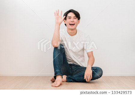 A young Asian man sitting cross-legged in the living room and waving (Men's Beauty) A young Asian man sitting cross-legged in the living room and waving (Men's Beauty) 133429573