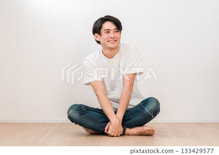 一位面帶微笑的年輕亞洲男子盤腿坐在客廳裡(男性之美) 一位面帶微笑的年輕亞洲男子盤腿坐在客廳裡(男性之美) 133429577