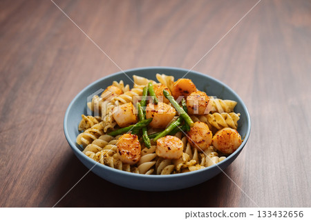 Fusilli pasta with scallops and asparagus in blue bowl on walnut wood surface with copy space Fusilli pasta with scallops and asparagus in blue bowl on walnut wood surface with copy space 133432656