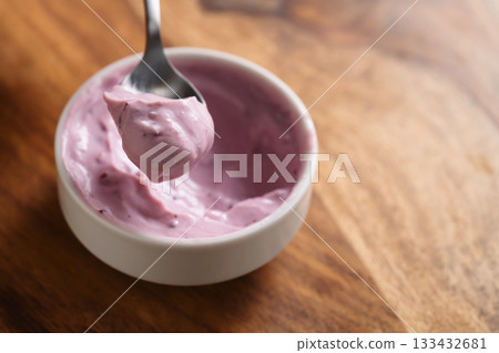 eating blueberry yogurt from white bowl on wood table 133432681