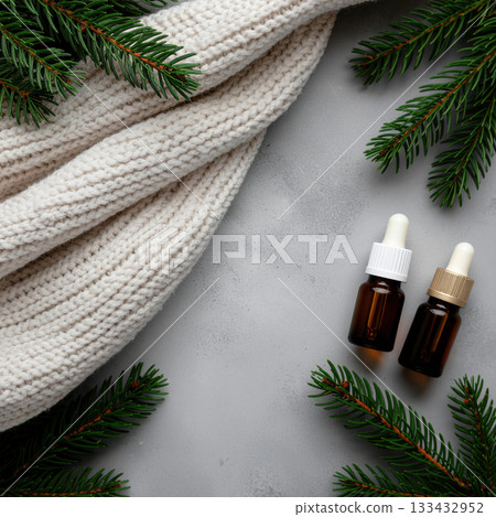 Cozy winter scene with knitted sweater, essential oil bottles, and pine branches on gray background Cozy winter scene with knitted sweater, essential oil bottles, and pine branches on gray background 133432952