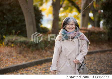 A calm everyday scene of a senior woman walking along a road lined with autumn leaves. Image of travel, sightseeing, and shopping. A calm everyday scene of a senior woman walking along a road lined with autumn leaves. Image of travel, sightseeing, and shopping. 133433344