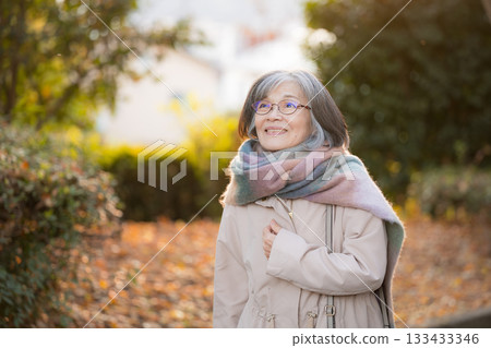 A calm everyday scene of a senior woman walking along a road lined with autumn leaves. Image of travel, sightseeing, and shopping. A calm everyday scene of a senior woman walking along a road lined with autumn leaves. Image of travel, sightseeing, and shopping. 133433346