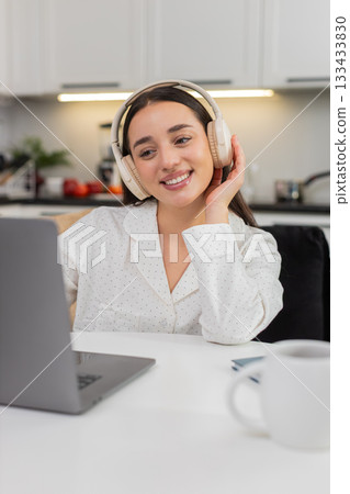 Young woman types on laptop in headphones smiles nods to rhythm music plays typing client email live 133433830
