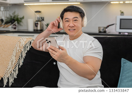 Asian man with wireless headphones enjoys playlist relaxes closes eyes rocks gently and smiles calm 133433847