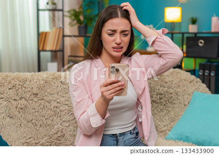 Young woman frowning at smartphone after contest loss shows sad reaction and very strong frustration 133433900