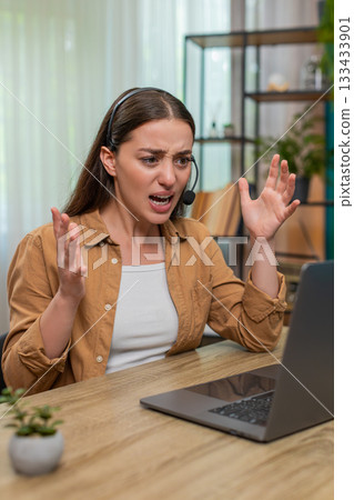 Young woman angry on laptop headset chat venting frustration shows intense tension during support Young woman angry on laptop headset chat venting frustration shows intense tension during support 133433901