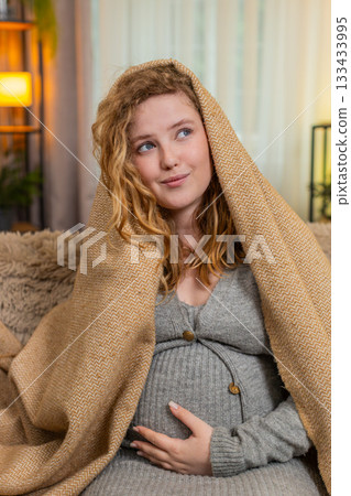 Pregnant young woman wrapped in warm blanket at home gently hugging belly cozy and comforting moment Pregnant young woman wrapped in warm blanket at home gently hugging belly cozy and comforting moment 133433995