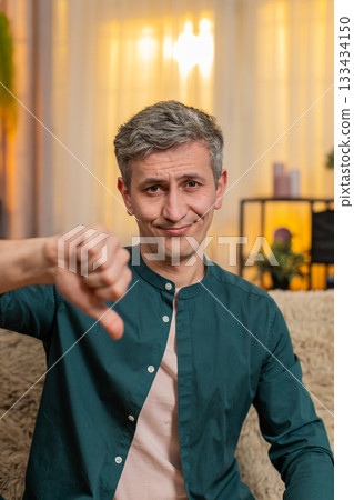 Young man shows thumbs down gesture with serious expression showing disapproval or disagreement 133434150