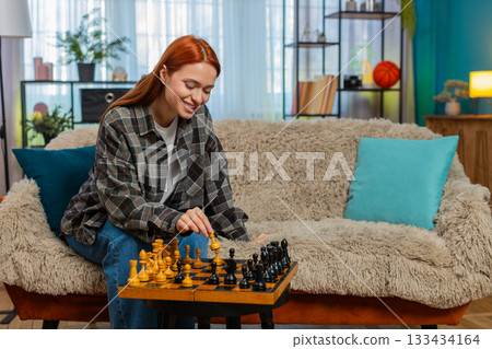 Woman on sofa playing chess against herself smiling having fun with playful split personality mood 133434164