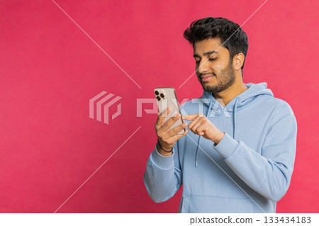 Happy Indian young man browsing social media smiling typing message on smartphone engaging working 133434183