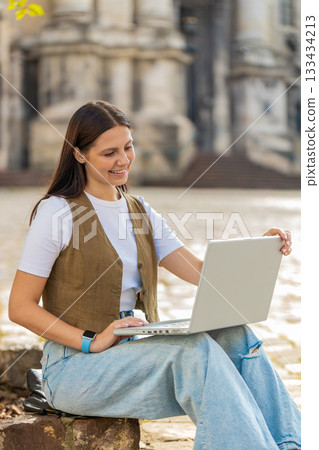 Caucasian young woman freelancer working online distant job with laptop sitting on city town street 133434213