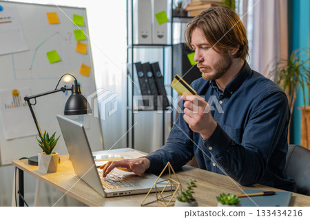 Concentrated businessman using bank credit card and laptop for online shopping payments at office 133434216