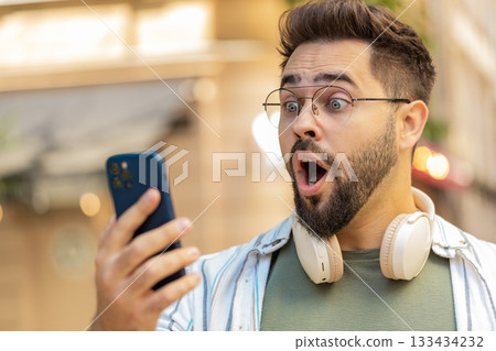 Upset young man using smartphone typing browsing, loses becoming shocked bad news on city street 133434232