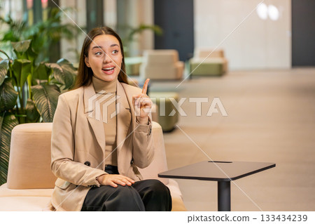 Thoughtful clever woman make gesture raises finger came up with creative plan in office lobby Thoughtful clever woman make gesture raises finger came up with creative plan in office lobby 133434239