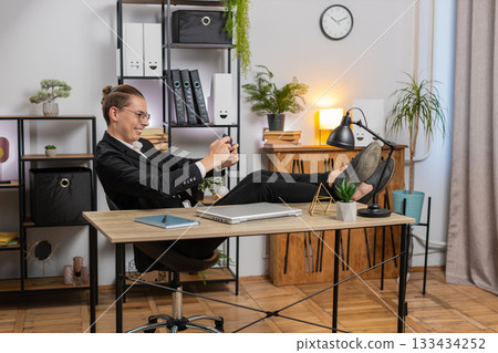 Excited young businessman playing shooter or racing video games on smartphone sitting at desk 133434252