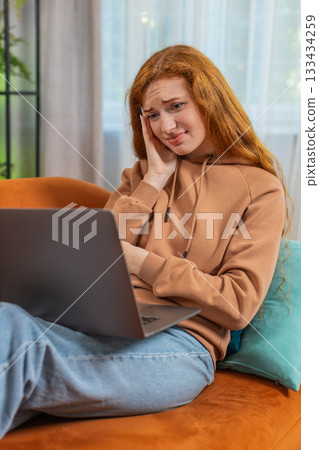 Upset young Caucasian young woman sitting on sofa at home using laptop having anxiety and stress 133434259