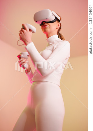 Female gamer in VR glasses against illuminated background Female gamer in VR glasses against illuminated background 133434664