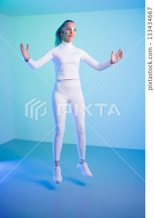 Female in smartglasses jumping against blue background Female in smartglasses jumping against blue background 133434667