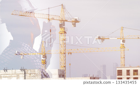 A construction worker in safety gear is seen giving instructions on a walkie-talkie against a backdrop of a construction site with construction cranes. They are responsible for organizing the A construction worker in safety gear is seen giving instructions on a walkie-talkie against a backdrop of a construction site with construction cranes. They are responsible for organizing the 133435455
