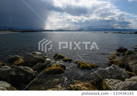 Glistening waters reflect the shifting skies over rocky shores twilight with storm clouds distance Glistening waters reflect the shifting skies over rocky shores twilight with storm clouds distance 133436183