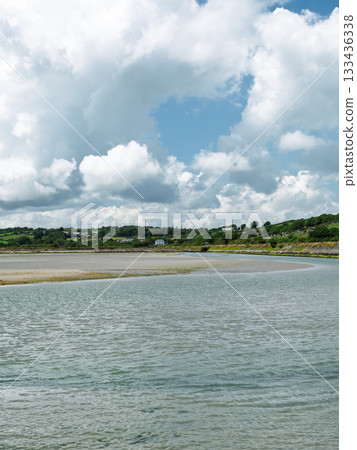 Expansive water stretches towards a sandy shore, framed by rolling green hills and a serene, cloud-dotted sky. Expansive water stretches towards a sandy shore, framed by rolling green hills and a serene, cloud-dotted sky. 133436338