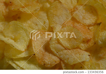 Crispy golden potato chips scattered on a white plate, inviting snack time bliss 133436356