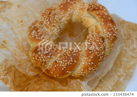 Freshly baked sesame bread ring resting on delicate parchment paper, showcasing golden hues and inviting texture 133436474
