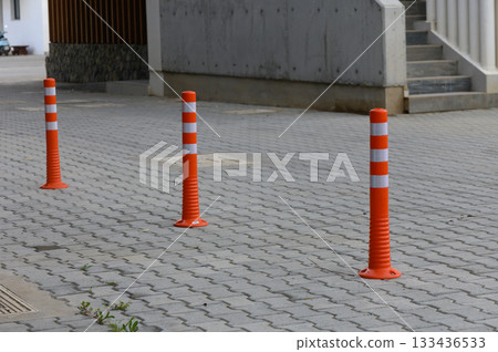 Bright orange traffic cones line the walkway, guiding pedestrians and enhancing safety in an urban setting during the daylight hours Bright orange traffic cones line the walkway, guiding pedestrians and enhancing safety in an urban setting during the daylight hours 133436533