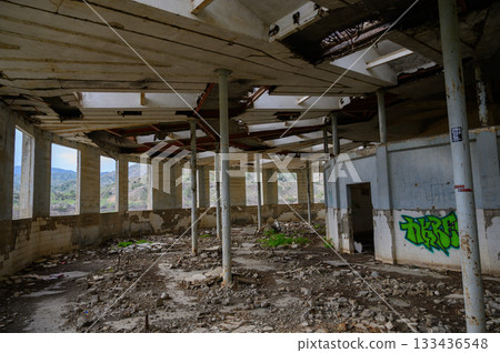 Exploring an eerie abandoned building nestled in nature's embrace with sunlight filtering through shattered windows 133436548