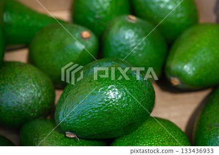 Fresh avocados stacked in natural light at a local market, showcasing their rich green color and smooth texture Fresh avocados stacked in natural light at a local market, showcasing their rich green color and smooth texture 133436933