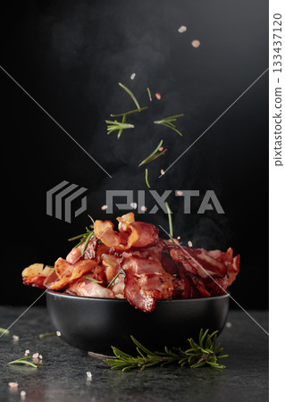 Fried bacon in a black dish, sprinkled with rosemary and pink salt. 133437120