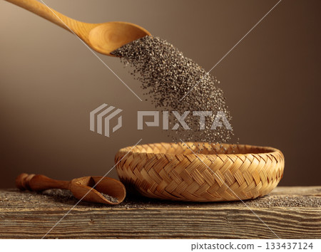 Chia seeds are poured into a wicker bowl. 133437124