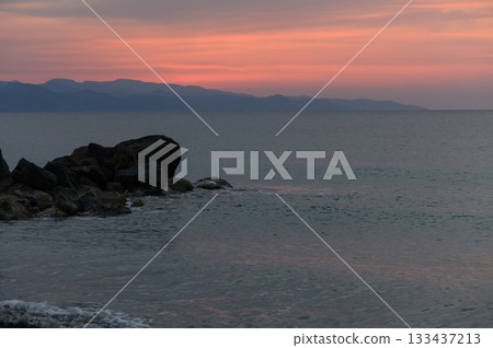 Calming twilight waves and vibrant sky colors at coastal rocks under a serene dusk in an idyllic seaside location 133437213