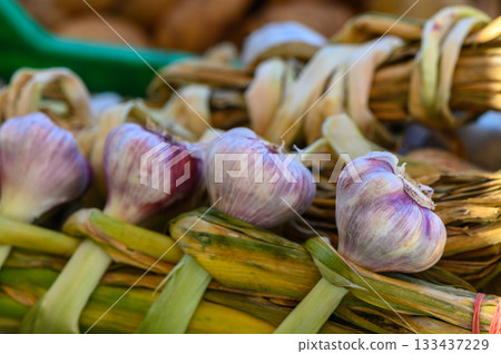 Vibrant garlic bulbs woven into a rustic basket at a lively farmers market in late summer 133437229