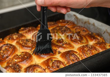 Baking a delicious batch of freshly glazed cinnamon rolls with nuts on a cozy afternoon Baking a delicious batch of freshly glazed cinnamon rolls with nuts on a cozy afternoon 133437385