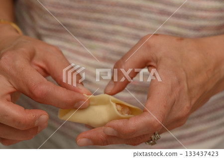 Skillful hands create delicate dumplings filled with savory goodness during a cooking session in a cozy kitchen Skillful hands create delicate dumplings filled with savory goodness during a cooking session in a cozy kitchen 133437423
