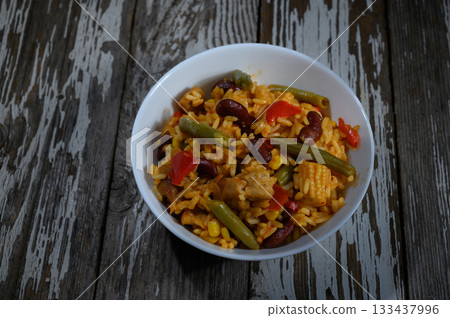 Colorful rice dish brimming with vegetables and beans evokes a sense of comfort and warmth on a rustic wooden table 133437996