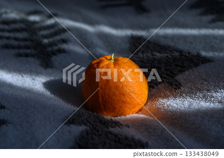 Bright orange mandarin resting on a cozy blanket in soft morning light Bright orange mandarin resting on a cozy blanket in soft morning light 133438049