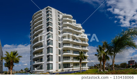 Modern architectural marvel shines under a bright blue sky with palm trees swaying gently in the breeze at a coastal location 133438066