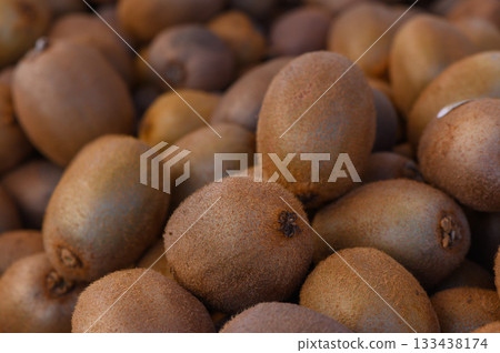 Fresh kiwi fruits piled high at a vibrant market, showcasing their fuzzy texture and earthy tones in a sunny setting Fresh kiwi fruits piled high at a vibrant market, showcasing their fuzzy texture and earthy tones in a sunny setting 133438174
