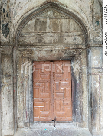 Ancient wooden double door set within red sandstone archway featuring intricate carvings, weathered textures, and Mughal-era architectural details in historical monument 133438230