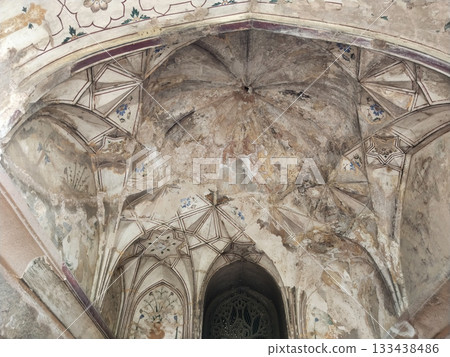 Intricately carved and painted vaulted ceiling of Mughal-era sandstone archway featuring faded floral motifs, geometric star patterns, and centuries-old weathered textures 133438486