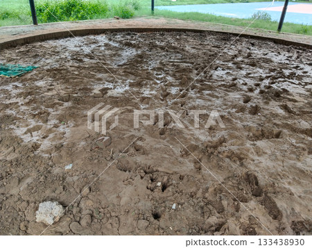 Muddy circular sports arena with wet soil surface and brick boundary in open park, traditional outdoor ground prepared for local games or wrestling, natural earth field surrounded by green landscape Muddy circular sports arena with wet soil surface and brick boundary in open park, traditional outdoor ground prepared for local games or wrestling, natural earth field surrounded by green landscape 133438930