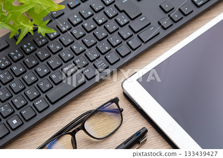 桌上放著平板電腦、鍵盤、眼鏡和原子筆。 133439427