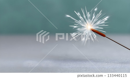 Close-up lit sparkler bursting with bright sparks on a soft teal background 133440115