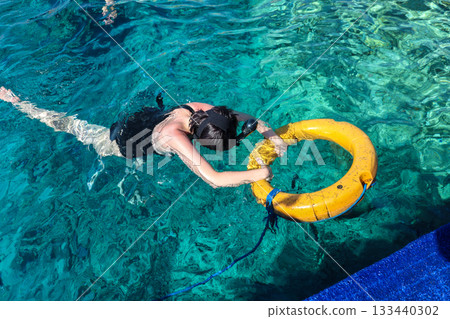 A woman looks at the underwater world with her head in the water and holding onto a lifebuoy A woman looks at the underwater world with her head in the water and holding onto a lifebuoy 133440302