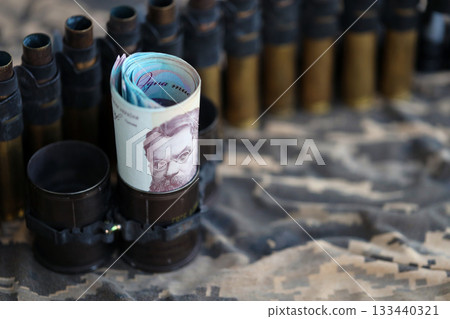 Ukrainian army machine gun belt shells and bunch of hryvnia bills on military uniform. Payments to soldiers of the Ukrainian army, salaries to the military. War in Ukraine Ukrainian army machine gun belt shells and bunch of hryvnia bills on military uniform. Payments to soldiers of the Ukrainian army, salaries to the military. War in Ukraine 133440321