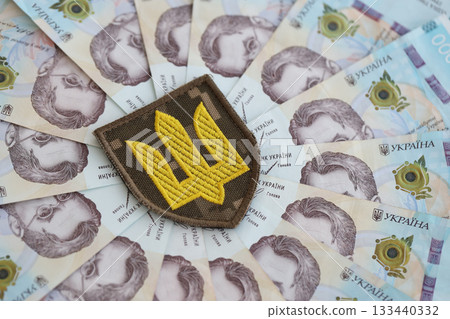 Ukrainian military symbol and hryvnia bills. Payments to soldiers of the Ukrainian army, salaries to the military. War in Ukraine Ukrainian military symbol and hryvnia bills. Payments to soldiers of the Ukrainian army, salaries to the military. War in Ukraine 133440332